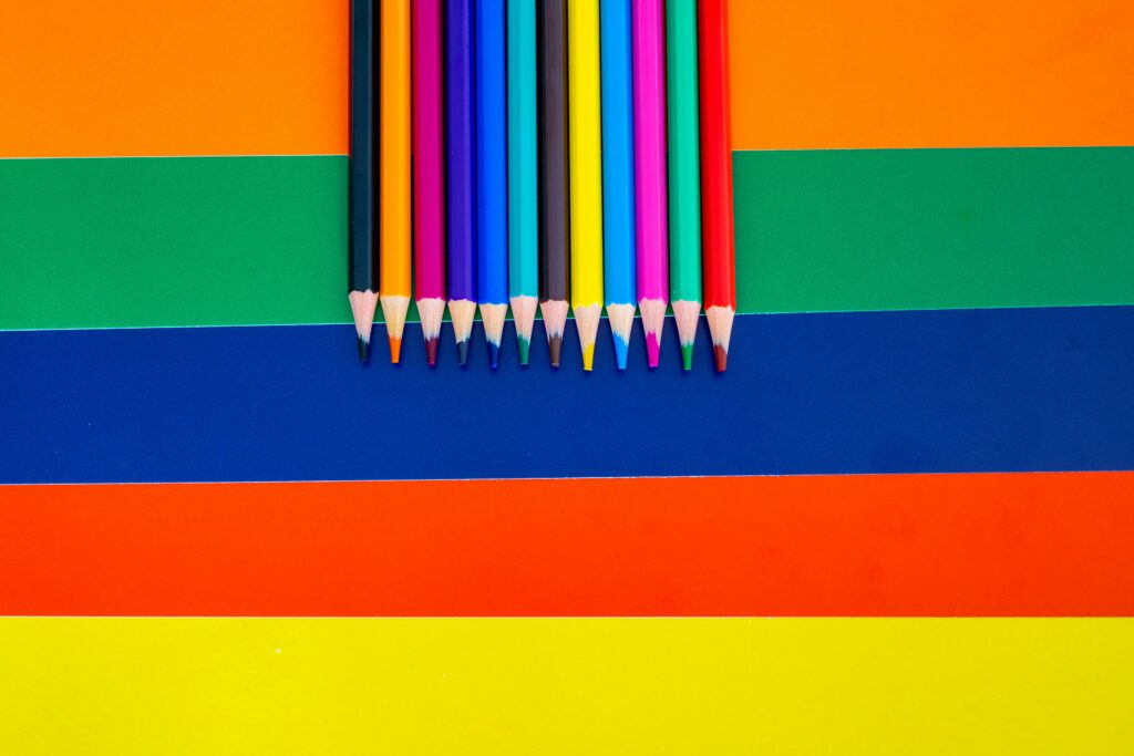 A collection of colored pencils arranged on a bright striped background, showcasing vivid rainbow hues.