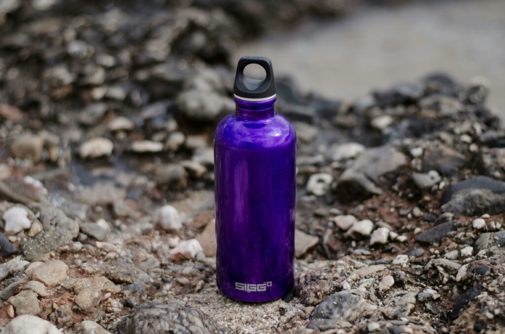 Close-up of a purple water bottle on rocky ground, perfect for outdoor adventures.
