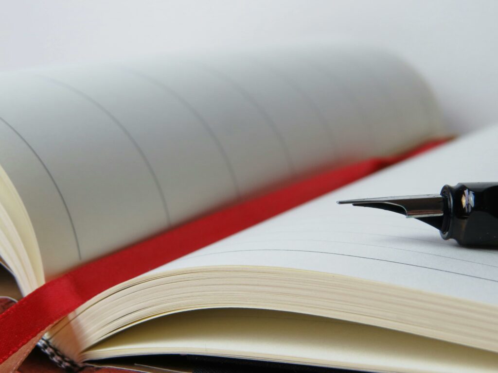 Close-up of a fountain pen resting on an open lined notebook with a red bookmark.