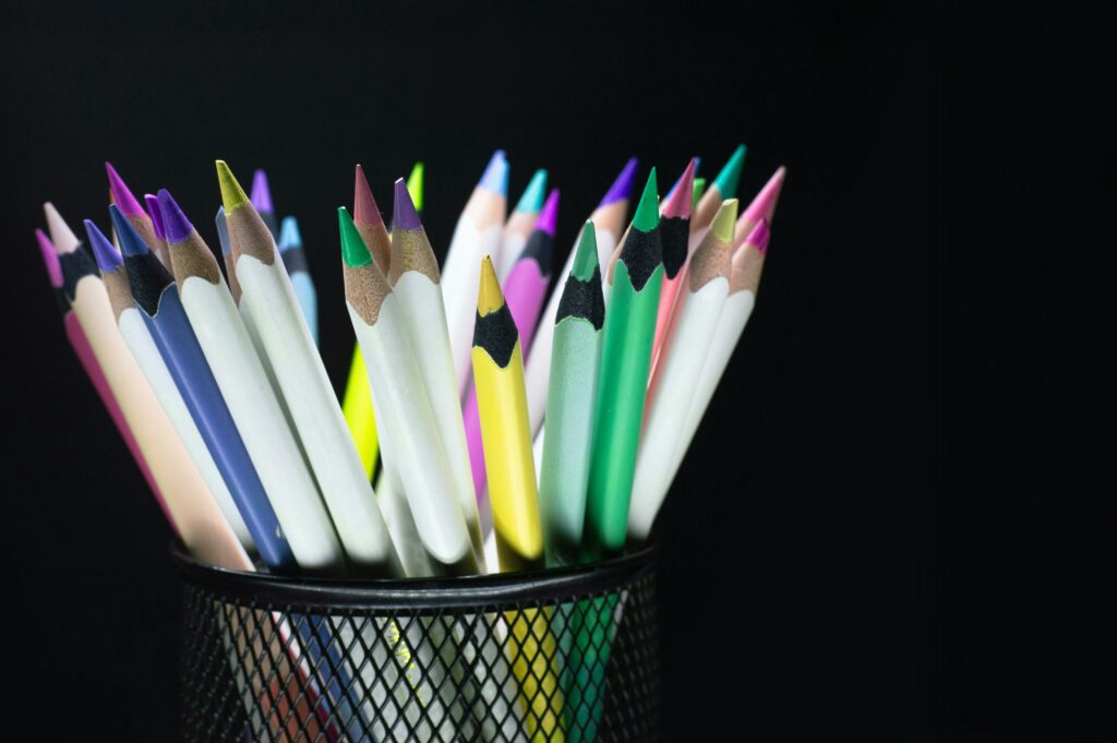 Assorted colorful pencils organized in a black mesh pencil holder against a dark backdrop.