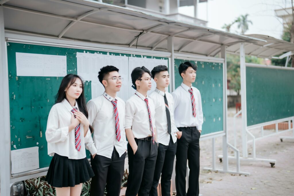 A group of students in uniform standing by the school bulletin board outdoors.