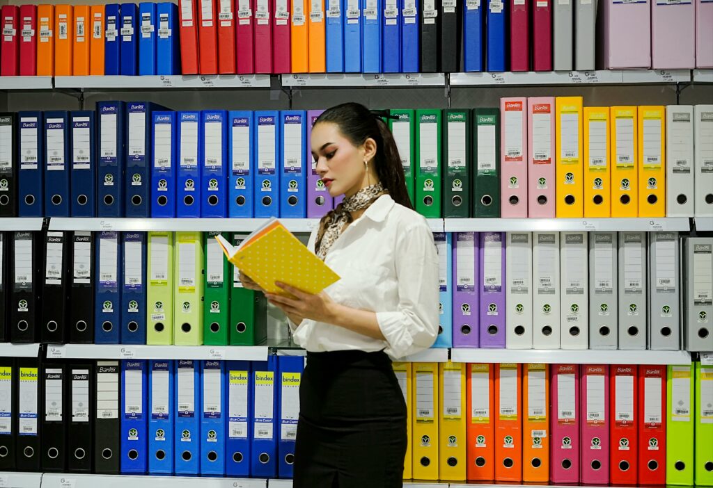A young woman reads a file in front of a vibrant array of office binders.
