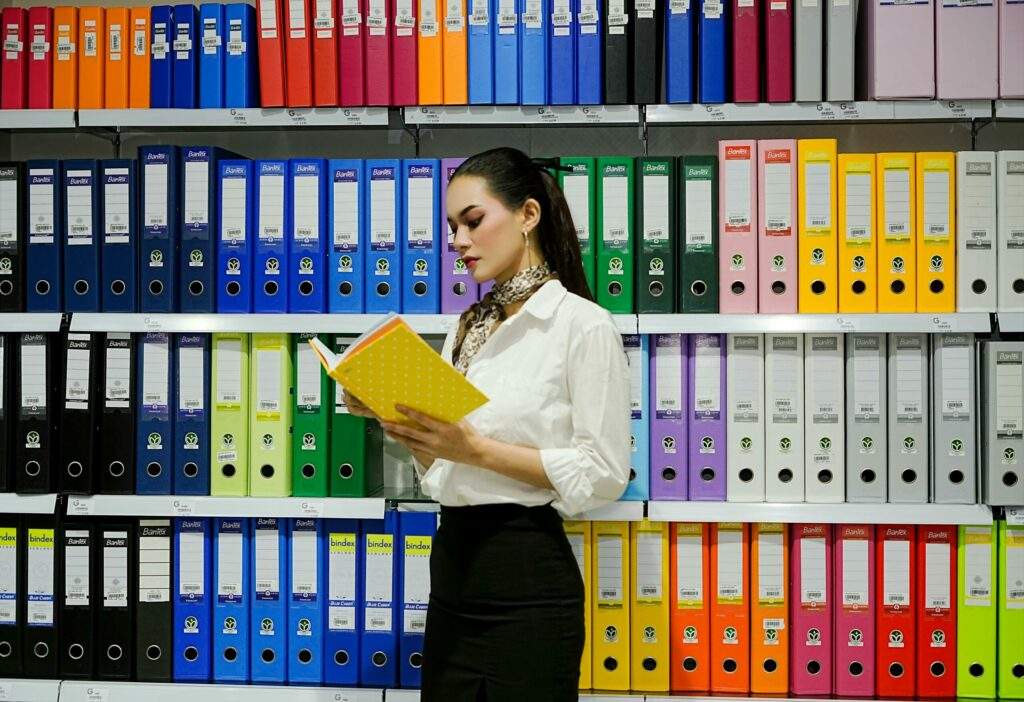 A young woman reads a file in front of a vibrant array of office binders.