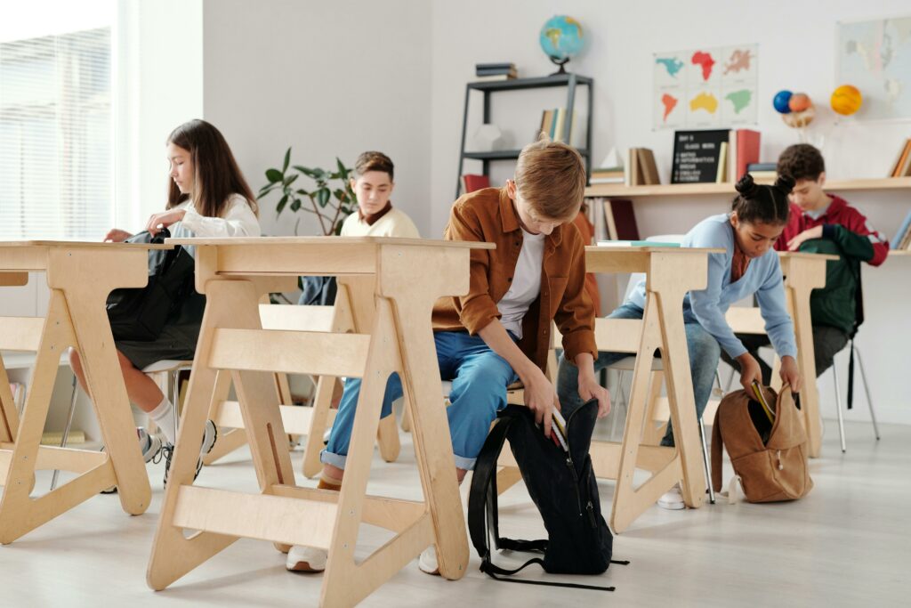 Teen students organizing backpacks in a bright classroom setting.