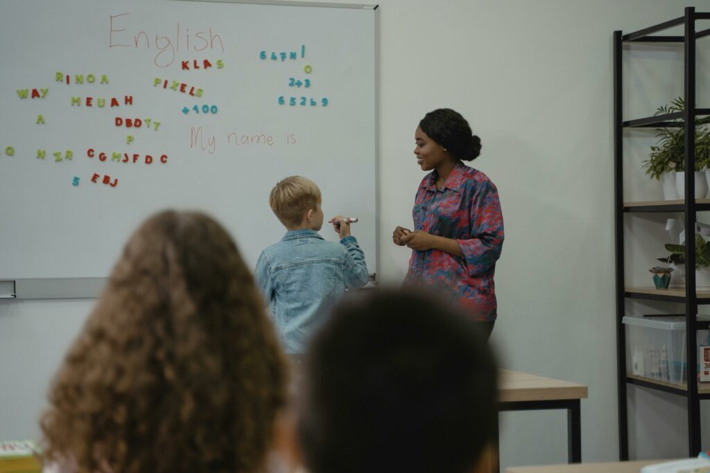 A teacher engages students in an interactive English lesson using a whiteboard and magnetic letters.
