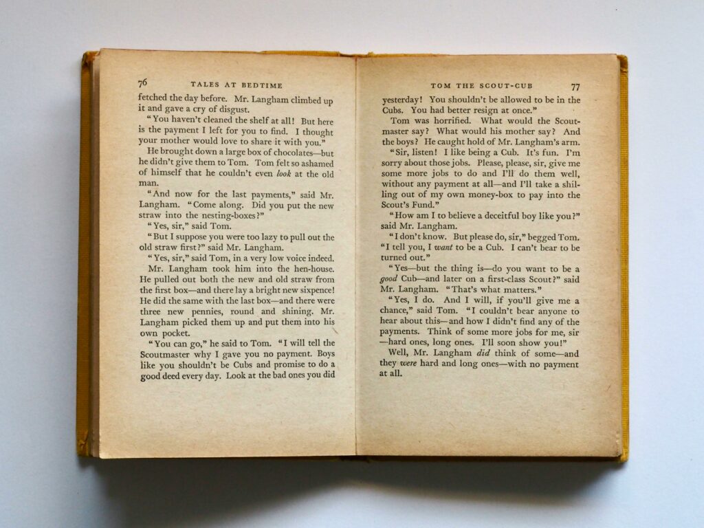 Vintage book opened to pages 76-77, displaying classic literature text in soft lighting.