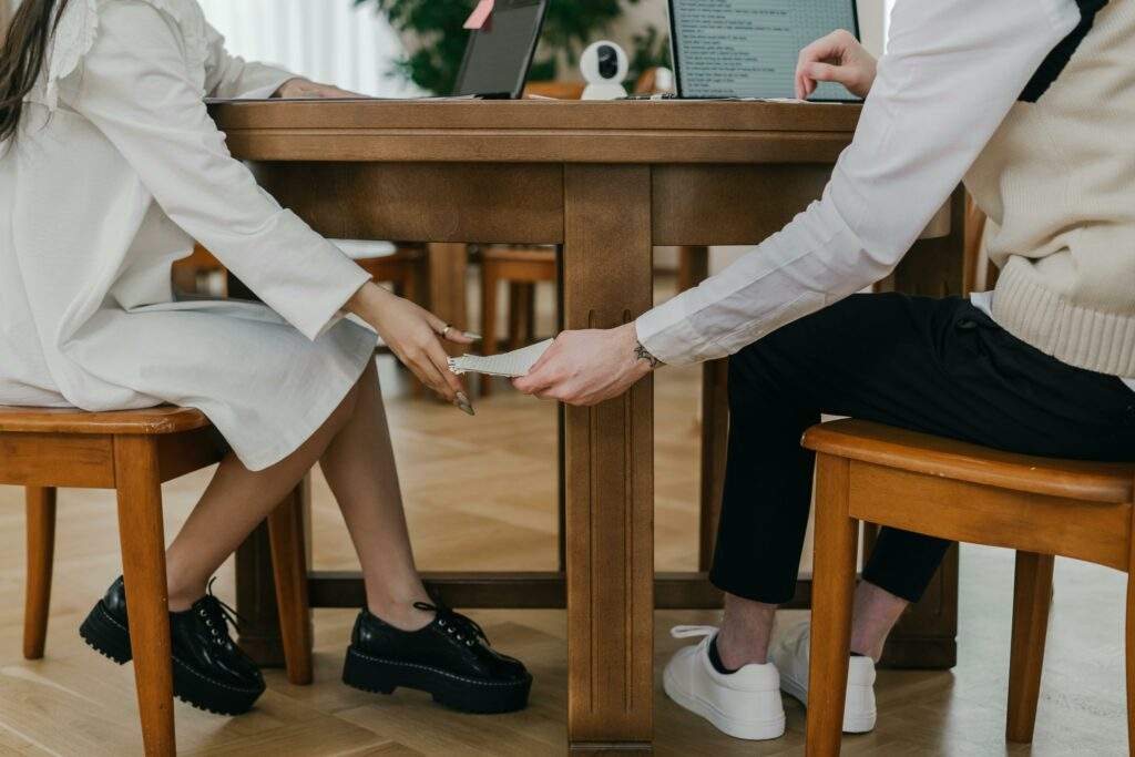 Two students covertly passing notes under a table during an exam indoors.